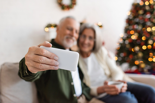 middle aged man taking selfie with wife near christmas tree on blurred background