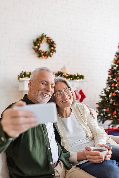 middle aged man taking selfie with happy wife near christmas tree at home