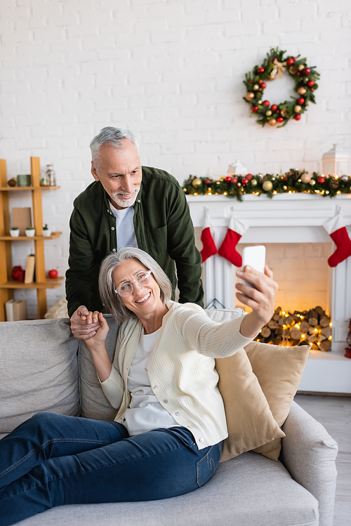 happy mature woman in glasses taking selfie with husband during christmas