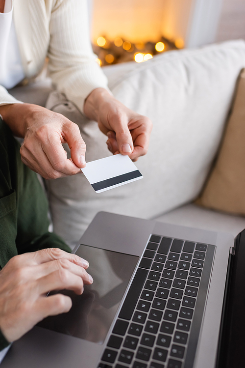 cropped view of mature man using laptop near wife with credit card during christmas holidays
