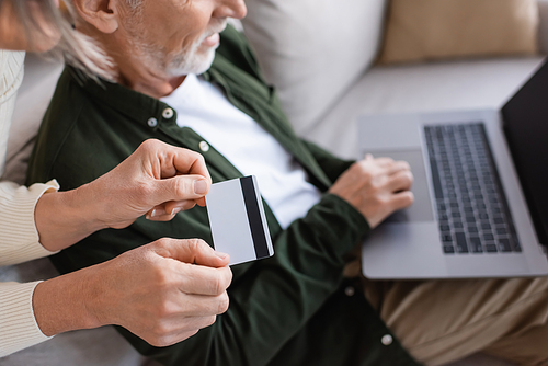 cropped view of smiling mature man using laptop near wife with credit card