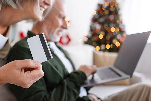 blurred mature man using laptop near happy wife with credit card during christmas