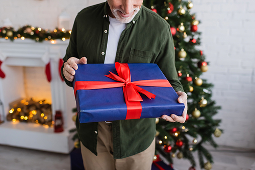 cropped view of happy and bearded middle aged man holding wrapped present near christmas tree