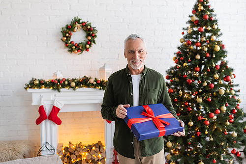 happy middle aged man holding wrapped present near decorated christmas tree