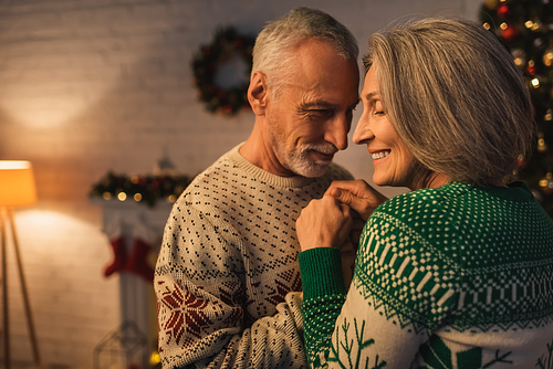 cheerful bearded man in festive sweater hugging smiling mature wife on christmas evening