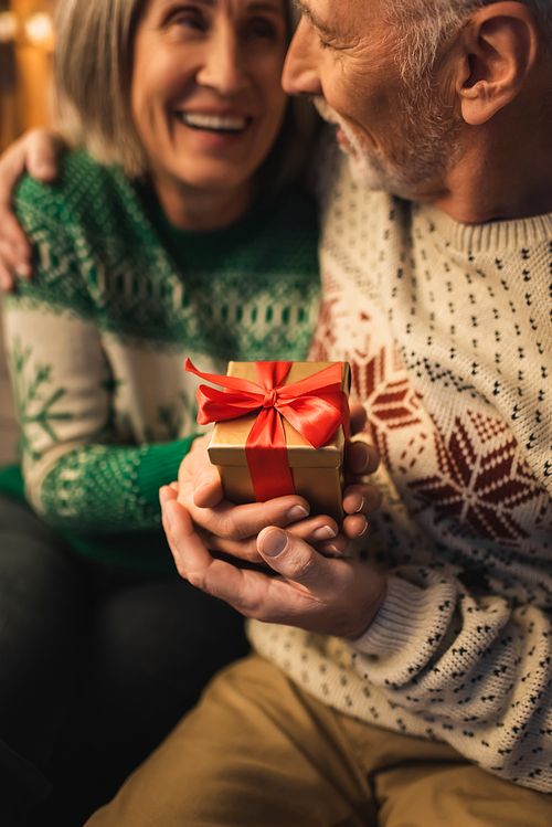 happy middle aged woman holding christmas present near smiling husband in sweater