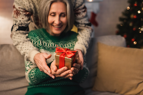 cheerful middle aged couple in festive sweaters holding christmas present in hands