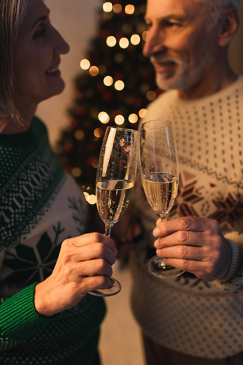blurred and cheerful middle aged couple in festive sweaters clinking glasses of champagne
