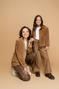 smiling mother and child in suede jackets and trendy clothes holding hands on beige background
