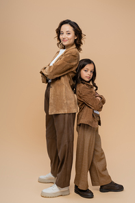 full length of fashionable mother and child standing back to back with crossed arms on beige background