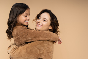 happy woman and girl in trendy autumn jackets embracing isolated on beige