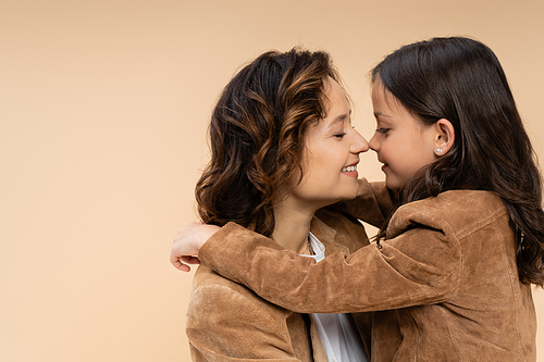 side view of child hugging happy mom in brown suede jacket isolated on beige