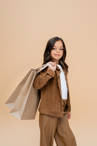 child in suede jacket and brown pants posing with shopping bags isolated on beige