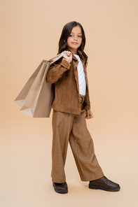 full length of girl in suede jacket and brown pants holding shopping bags on beige background