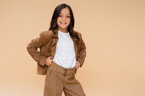 joyful kid in trendy autumn outfit standing with hands on hips isolated on beige