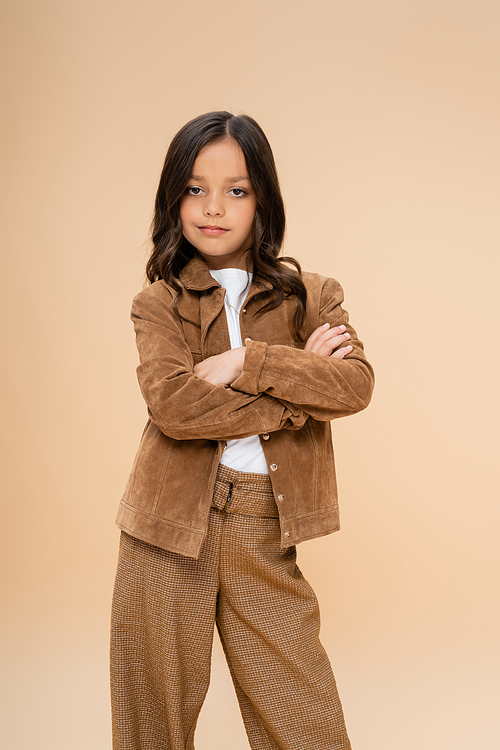 child in trendy autumn jacket and pants standing with crossed arms isolated on beige