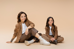 mother and daughter in fashionable autumn outfit sitting on beige background