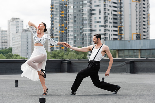 Smiling man holding hand of partner while dancing on roof of building outdoors