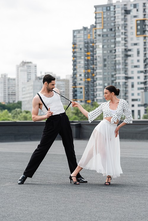 Brunette dancer in heels performing choreography with partner on rooftop