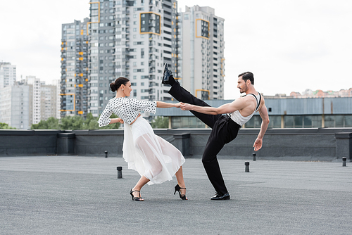 Side view of cheerful professional dancers moving on rooftop of building