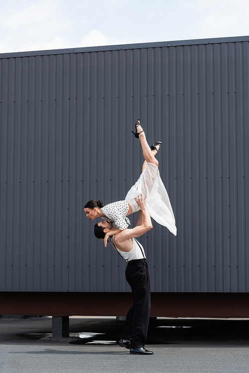 Side view of smiling dancer lifting partner in heels on roof of building outdoors