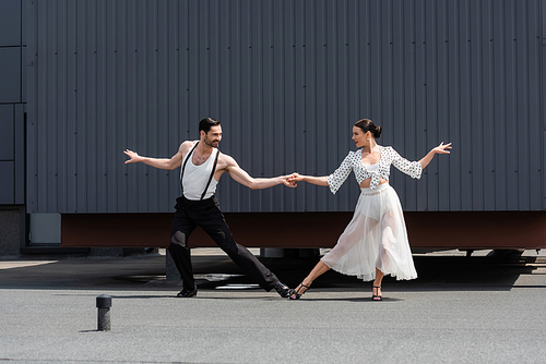 Cheerful ballroom dancers holding hands on roof of building outdoors