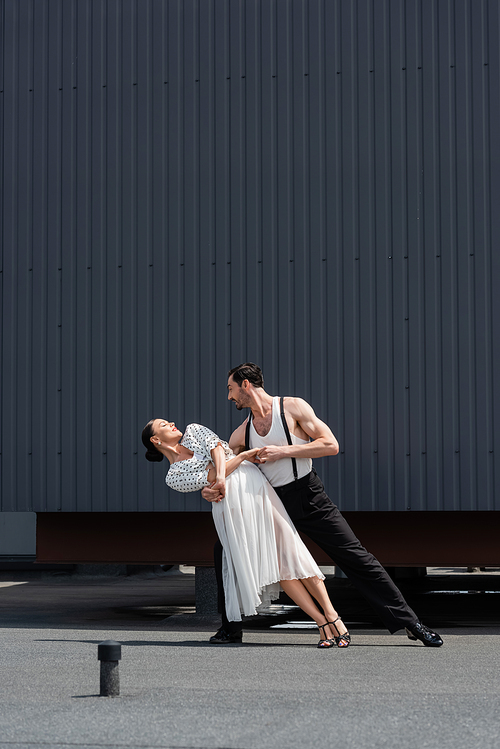 Side view of professional dancers moving and holding hands of roof of building outdoors