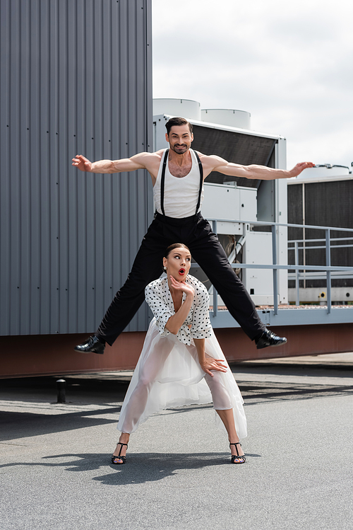 Smiling dancer jumping near shocked partner on roof of building outdoors