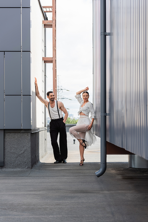 Smiling ballroom dancer standing near partner on rooftop of building outdoors