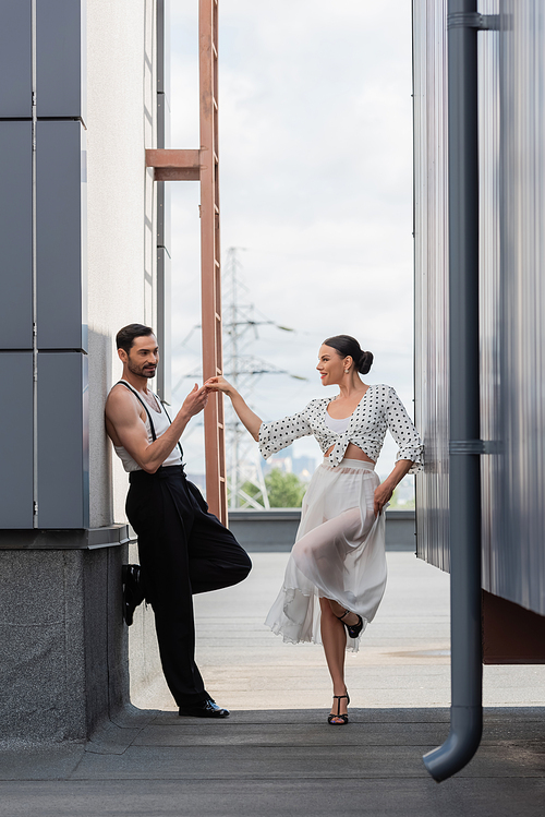 Smiling professional dancer touching hand of partner on rooftop of building outdoors