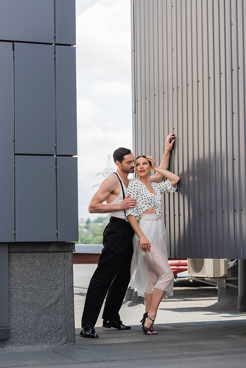 Dancer hugging smiling partner in heels and skirt on rooftop of building at daytime