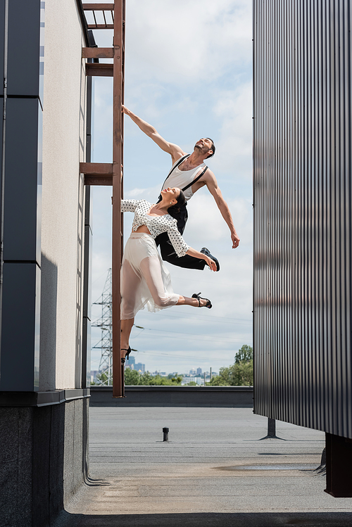 Positive dancers posing on ladder on rooftop of building at daytime