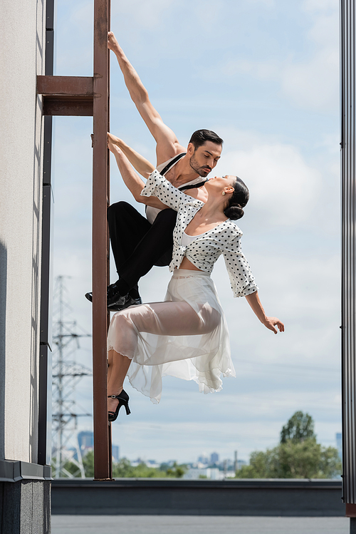 Professional dancers kissing while posing on ladder on rooftop of building at daytime