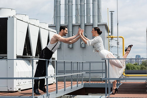 Side view of excited professional dancers giving high five on rooftop of building