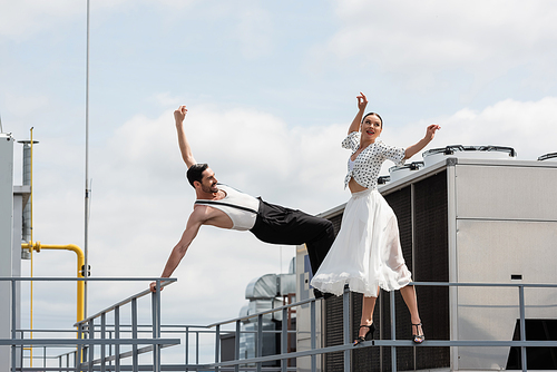 Cheerful professional dancers moving near railing on roof of building outdoors