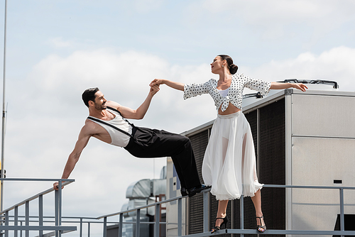 Side view of cheerful professional dancers holding hands near railing on rooftop of building outdoors