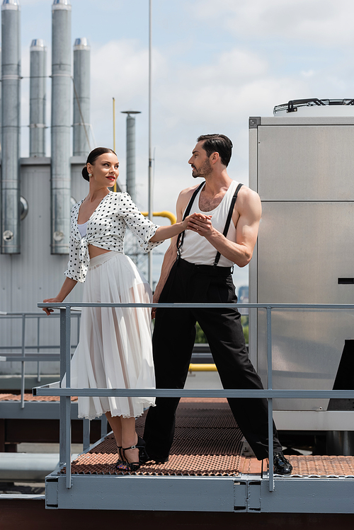 Stylish professional dancers holding hands near railing on roof of building outdoors