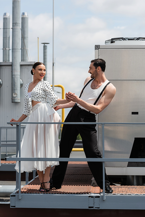 Cheerful dancers holding hands while moving near railing on roof of building outdoors