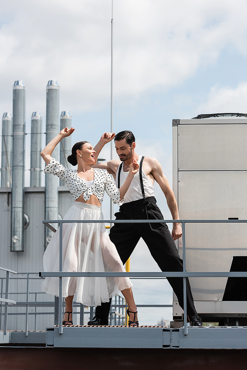 Cheerful and stylish dancer moving near partner on roof of building outdoors