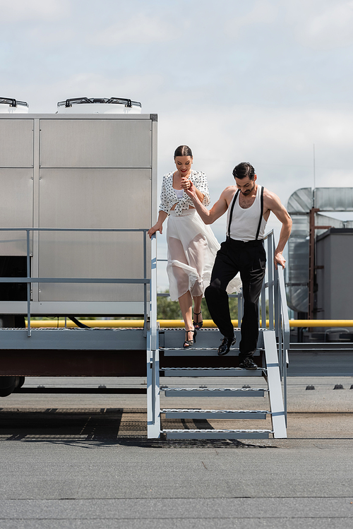 Stylish pair of dancers holding hands while walking on stairs on roof