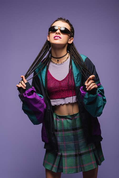 Young woman in vintage clothes and sunglasses standing isolated on purple