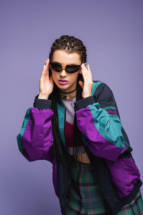 Stylish model in sunglasses and retro sports jacket isolated on purple