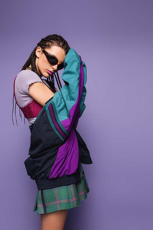 woman with braids posing in sunglasses with vintage style jacket isolated on purple