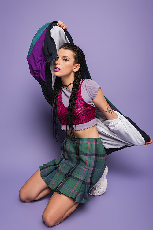 brunette woman in plaid skirt posing with vintage style jacket on purple background