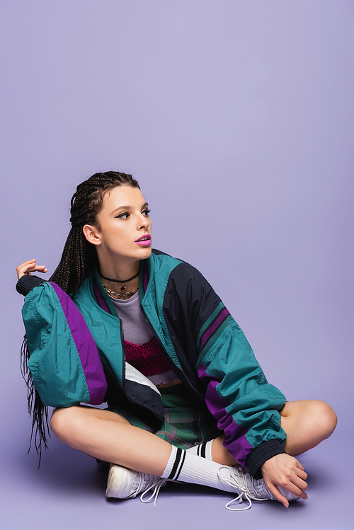 woman with braids sitting in nineties style jacket and looking away on purple background