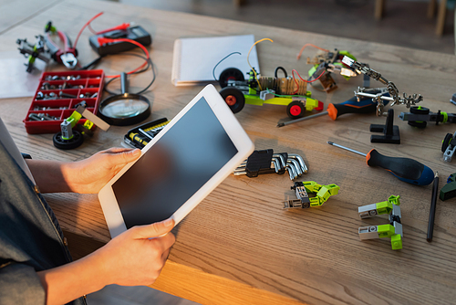 partial view of kid holding digital tablet with blank screen near tools and mechanical details on table