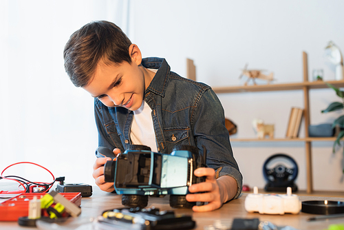 happy boy holding handmade car model near blurred parts on table