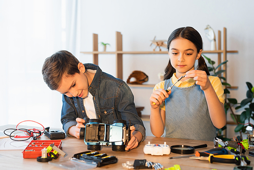 preteen girl holding screwdriver while boy assembling car model near mechanical parts on table