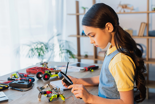 side view of girl with magnifier writing in notebook near mechanical parts of robotics model