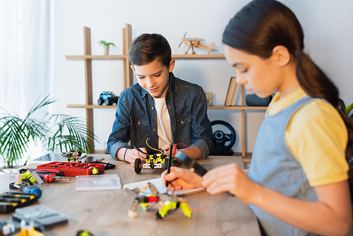 boy assembling robotics model near blurred girl with magnifier writing in notebook